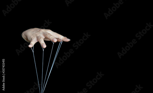 The female hand controls the doll with the fingers, using white threads attached to the fingers on a black isolated background. Close-up, banner, selective focus.