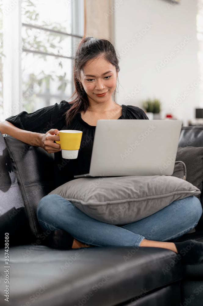 Young asian woman using laptop while sitting on a couch at home. Young asian woman using laptop while sitting on a couch at home.