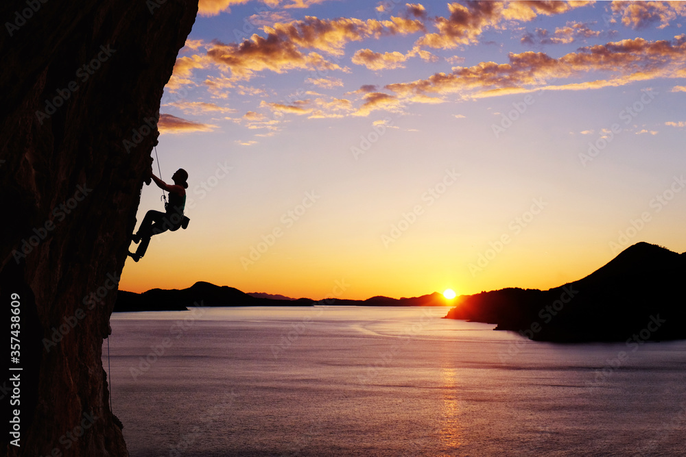 A silhouette of woman climbing on rock, mountain at sunset. Rock climber on a cliff