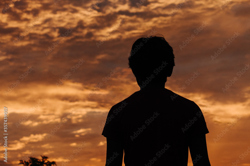 Silhouette of a kid in front of the beautiful dramatic sky during sunset Silhouette of a kid in front of the beautiful dramatic sky during sunset
