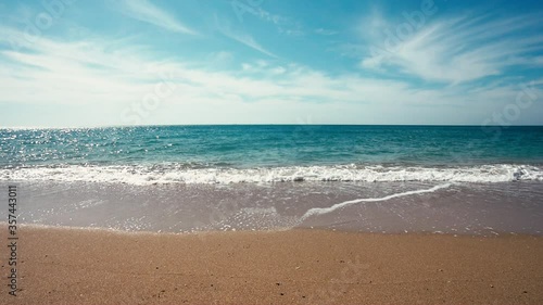 Calm turquoise waves of the ocean roll over the yellow sand against the background of beautiful white clouds in the blue sky