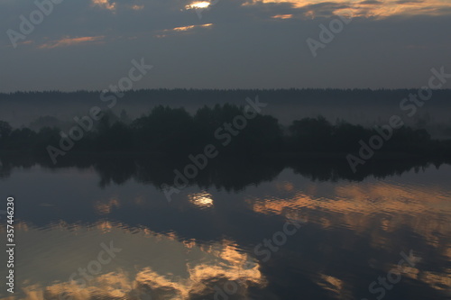 Beautiful night landscape. The reflected sky in the water of the lake with Golden clouds and a strip of black forest in the fog on the horizon line.Russia