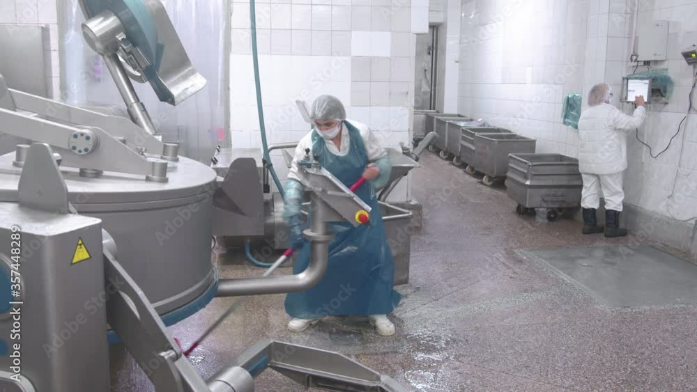 Worker washes the equipment with water from a hose at the enterprise. Sanitary cleaning of sausage production equipment at the enterprise. Worker washes the equipment with water from a hose at the enterprise. Sanitary cleaning of sausage production equipment at the enterprise.
