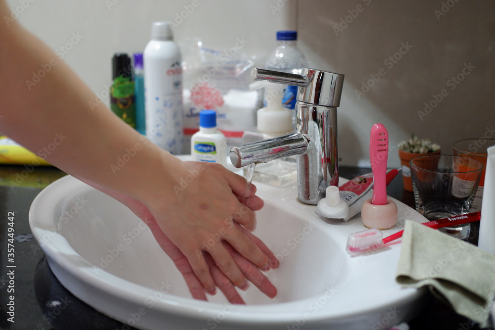 Light-skinned Asian woman rinsing hands in the bathroom sink. Shows hygiene and cleanliness for virus or bacterial spread prevention Light-skinned Asian woman rinsing hands in the bathroom sink. Shows hygiene and cleanliness for virus or bacterial spread prevention