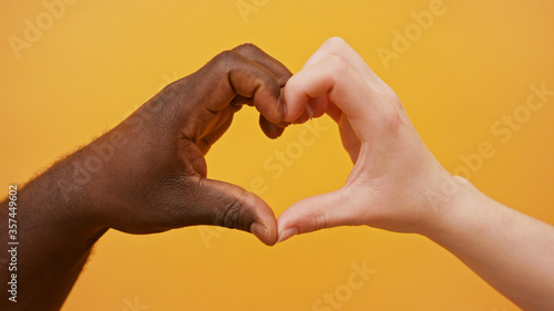 black and white hands forming heart shape together isolated on the orange background. Close up.