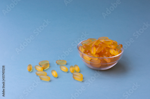 A lot of soft jelly capsules with fish oil as a source of Omega 3 in a transparent  bowl on blue background. Concept of health care and using biologically active additives.