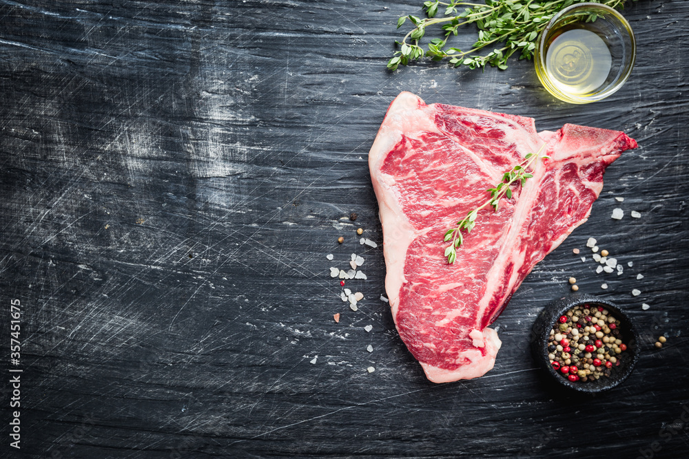 Raw T-bone Steak with fresh herbs and oil on black background, top view