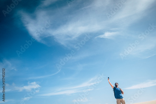 Standing man in outdoor leisure activity check phone internet signal to communicate - concept of internet phone device and communication time in the world - blue sky bckground