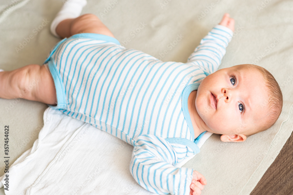 Little happy caucasian baby boy in striped clothes lying down on grey blanket ready to play.