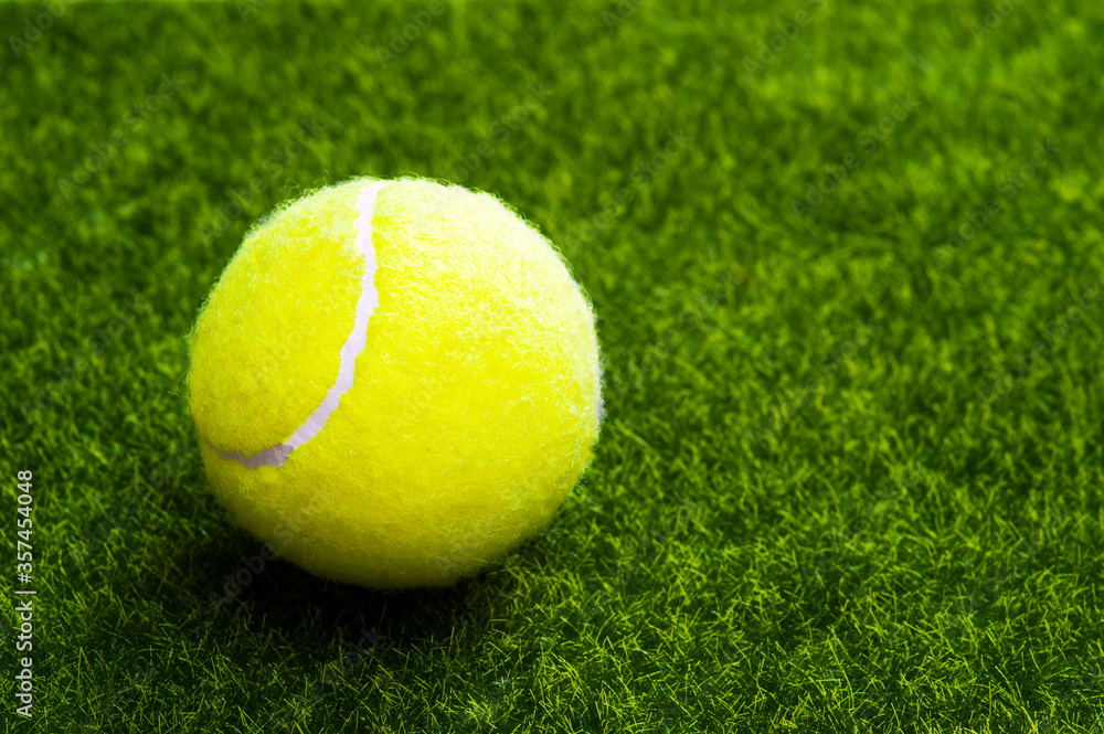 A tennis ball on a green artificial lawn with a copy of space.