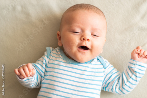 Obraz na płótnie Funny little 3 months old baby boy laughing and smiling with his eyes closed, lying down on grey blanket. Happy toddler in blue striped bodysuit. w salonie