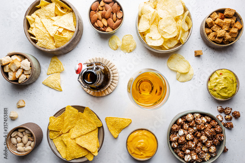 Veraity bowls of beer snacks and sauces on stone table. Nuts, chips, nachos, crackers. Top view with copyspace