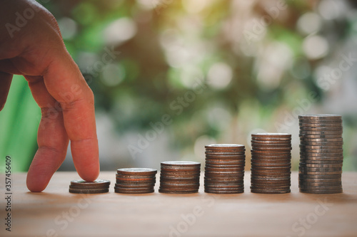 Male hand placed on money coins for stack growing with green bokeh background. Save Money concept for Financial, Investment and Business.