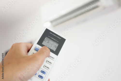 Hand with remote control directed on air conditioner inside the room