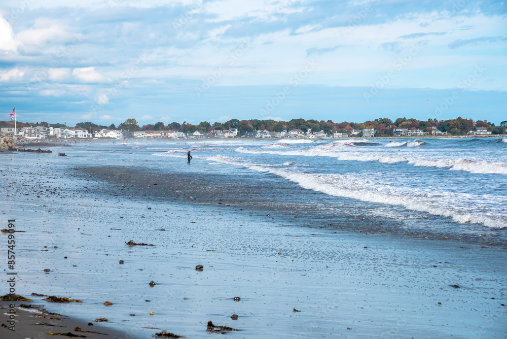 Distant view of people on a sandy beach and surfers in the sea on partly cloudy autumn day. Portsmouth, NH, USA.