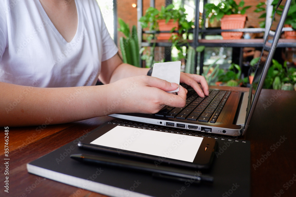 Fototapeta premium Cropped shot view of woman or man hands holding credit card, typing on laptop computer keyboard for internet banking and payment with phone. Online shopping.