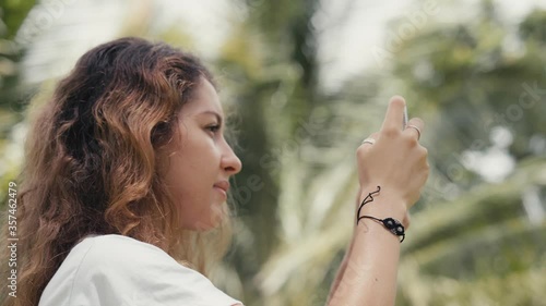 a woman is taking picture on her phone in the jungle while camera is rotating and moving around her. Close-up of full 360 degree rotation. Tracking Arc Shot