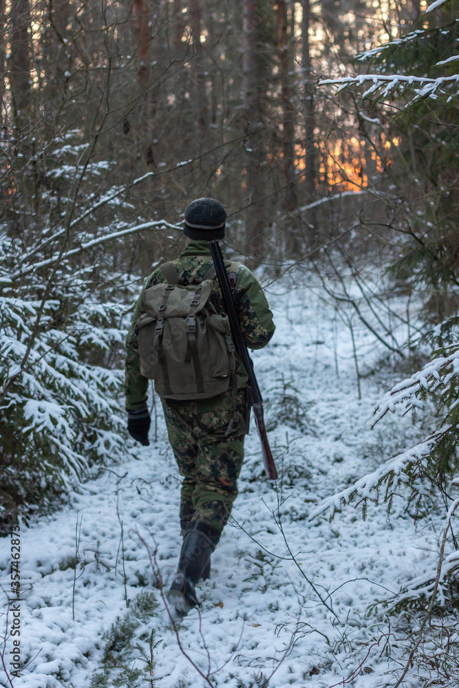 hunter with hunting gun walking on the forest road in winter