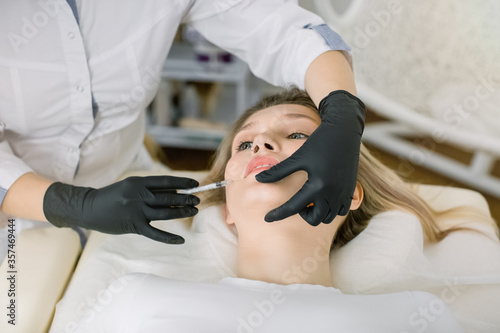 Lip Augmentation and Correction form. Cosmetology Treatment. Pretty young blond woman getting beauty injection for lips. Close up of hands of cosmetologist making injection in female lips.