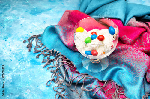 Ice cream with multicolor candies in a glass bowl standing on a colorful cloth and light blue background. Bright summer dessert concept.