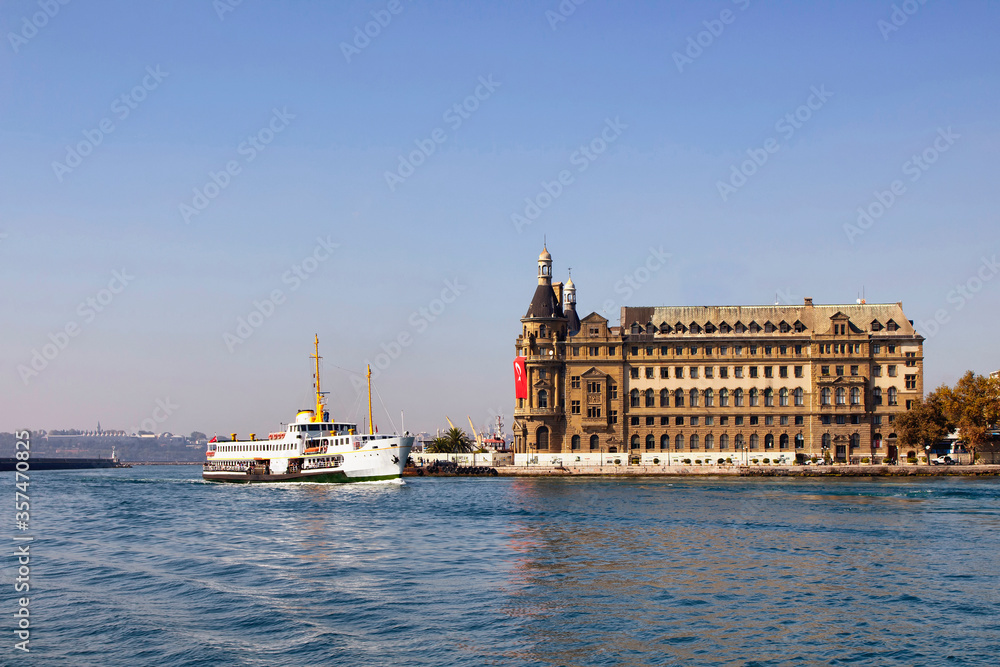 Traditional public ferry passes by historical train terminal named Haydarpasa