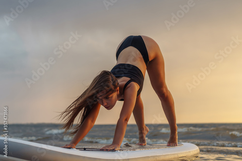 Young sexy woman surfer doing yoga on her sup board on the sunset. Rest at nature concept photo