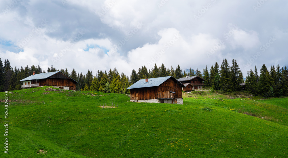 Fototapeta premium Beautiful view of scenic mountain landscape in the Alps with traditional old mountain chalet and fresh green meadows with blue sky and clouds in spring.