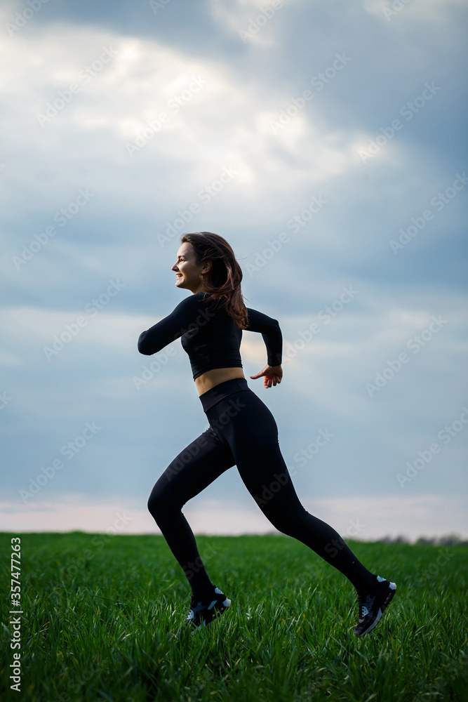 Young attractive brunette woman standing in nature, wearing black leggings and a black top. Summer day, green grass. Athletic body and healthy lifestyle. Young attractive brunette woman standing in nature, wearing black leggings and a black top. Summer day, green grass. Athletic body and healthy lifestyle.
