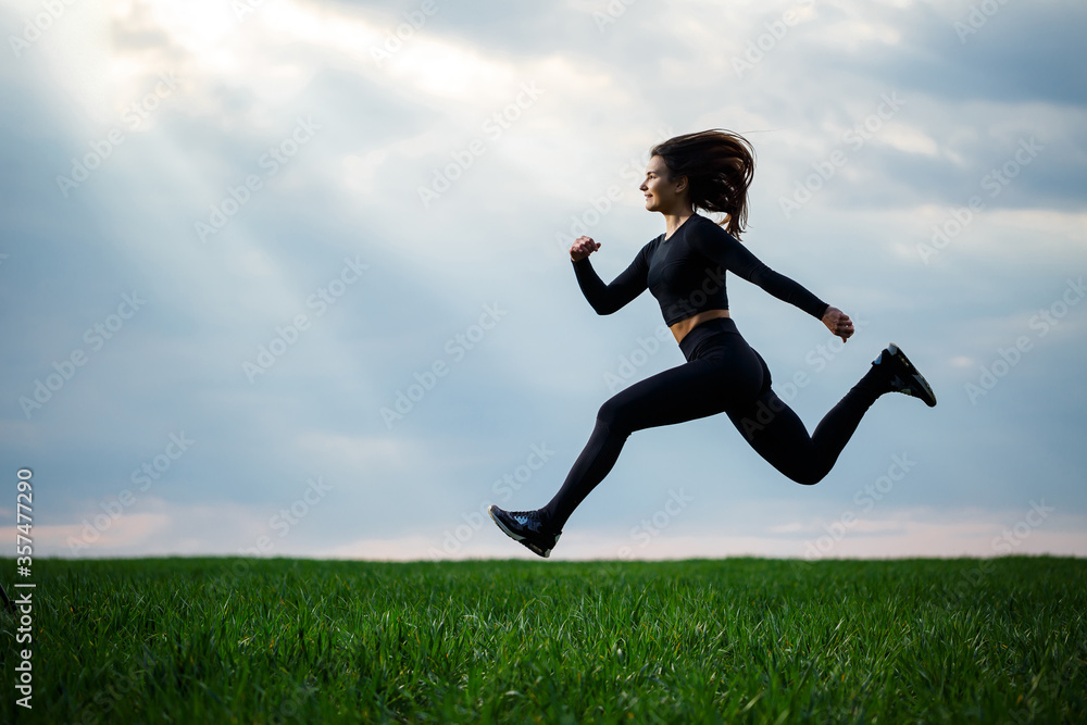 Young professional gymnast is jumping in nature against the blue sky. Girl athlete in a black top and black leggings does acrobatic exercises Young professional gymnast is jumping in nature against the blue sky. Girl athlete in a black top and black leggings does acrobatic exercises