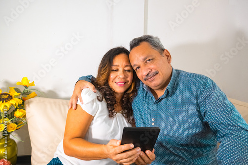 Portrait of happy senior couple relaxing on couch at home with tablet