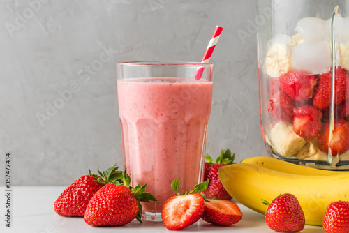 Glass of healthy smoothie or milkshake made of strawberry, banana, almond milk with blender and straw
