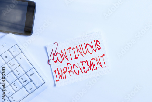 Handwriting text Continuous Improvement. Conceptual photo making small consistent improvements over time White pc keyboard with empty note paper above white background and mobile phone photo