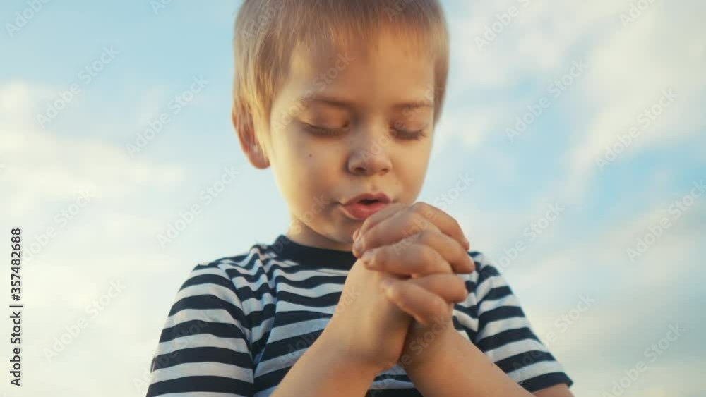 boy prays against a blue sky. child close-up concept faith religion and happy family. kid son jew crossed arms praying to god. worship lifestyle and gratitude for life and a happy childhood. catholic boy prays against a blue sky. child close-up concept faith religion and happy family. kid son jew crossed arms praying to god. worship lifestyle and gratitude for life and a happy childhood. catholic