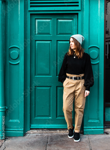 Attractive young female standing next to a blue door while wearing a hat
