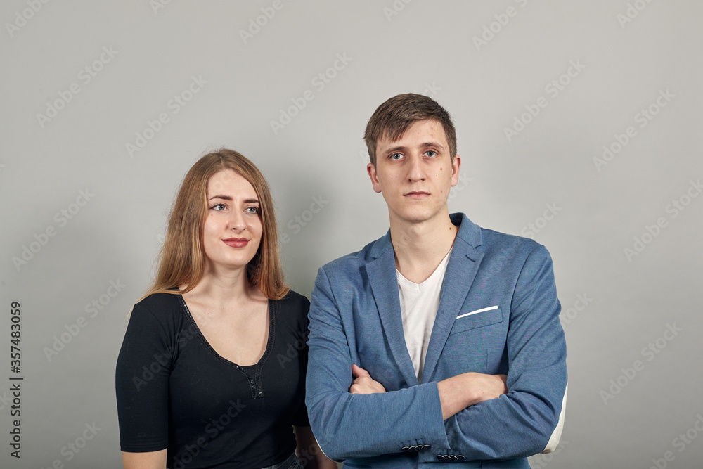 Closeup portrait looking straight at the camera, waist up of cheerful. Young attractive couple boyfriend girlfriend, two people, dressed black t-shirt, blue jacket, grey background, two people. Closeup portrait looking straight at the camera, waist up of cheerful. Young attractive couple boyfriend girlfriend, two people, dressed black t-shirt, blue jacket, grey background, two people.