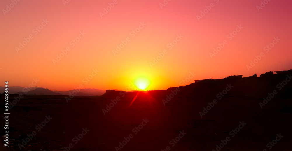 Dawn in the desert. The bright orange sun rises from behind the mountains. Nature background Dawn in the desert. The bright orange sun rises from behind the mountains. Nature background