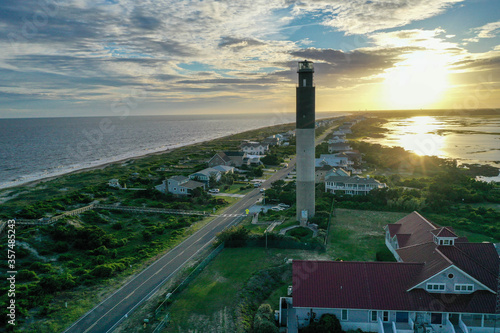 Looking down the coastline and waterway with the Oak Island Lighthouse in view. Sun setting behind the clouds behind the lighthouse. North Carolina beaches.