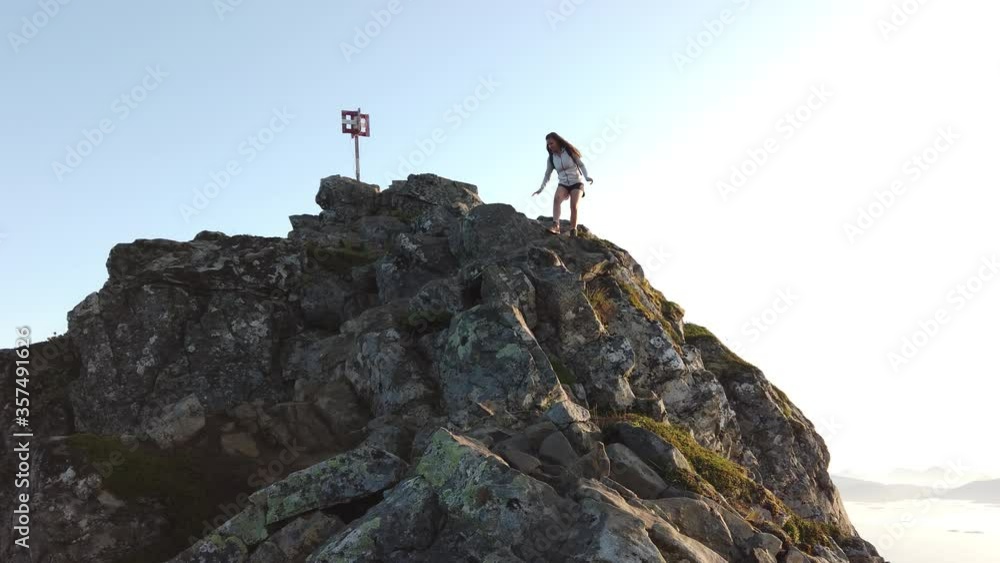 A young, fit woman is climbing down the big rocks and boulders of the peak of Festvågtind mountain with her backpack and hiking boots.