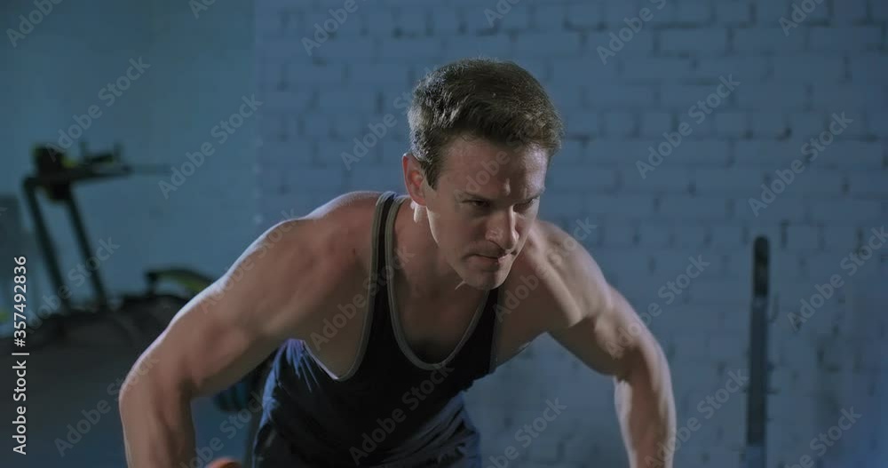 Muscular male athlete doing breeding hands with dumbbells to the side. Basic exercise for the muscles of the back. Tense look and torso muscles.
