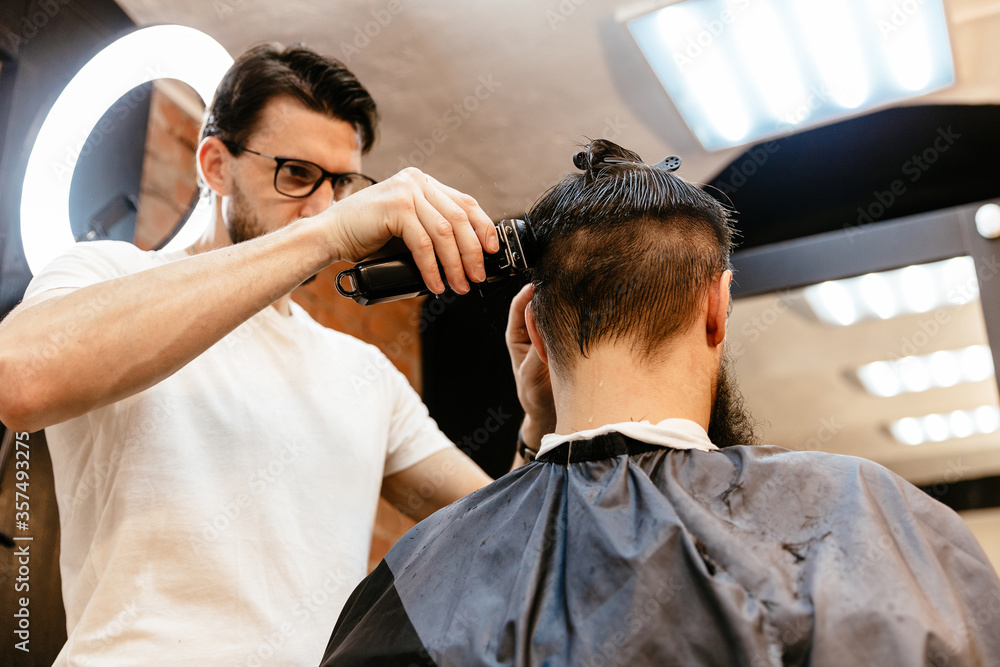 Grooming of real man. Rear view of young bearded man getting beard haircut at hairdresser while sitting in chair at barbershop Grooming of real man. Rear view of young bearded man getting beard haircut at hairdresser while sitting in chair at barbershop