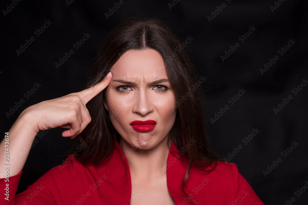 Emotional head shot portrait of a brunette caucasian woman in red dress and with red lips on black background. She make unhappy, dusgusting emotions