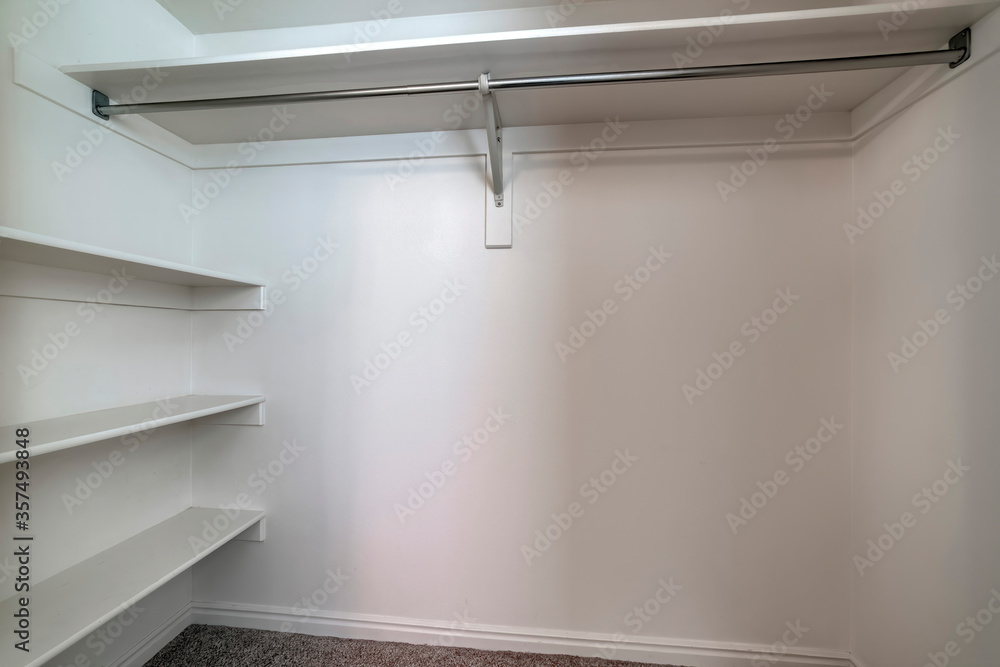 Empty walk in closet of new home with wall shelves and hanging clothes ...
