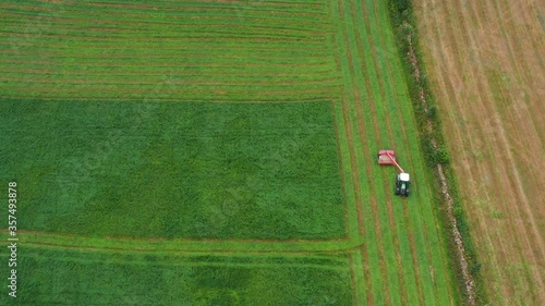 Aerial top-down view of a tractor cutting grass moving on beautiful fresh green field meadow pasture. the cut grass will be dried and become hay and then used as animal silage.