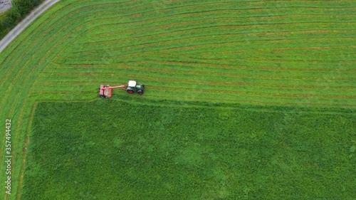 Aerial top-down view of a tractor cutting grass moving on beautiful fresh green field meadow pasture. the cut grass will be dried and become hay and then used as animal silage.