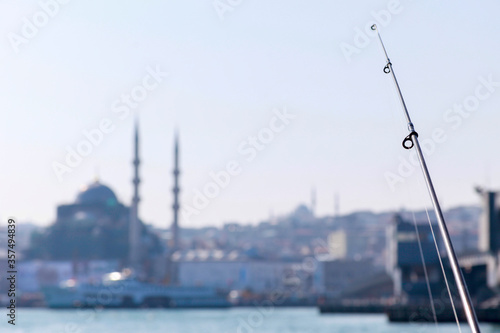 Fishing rod with a mosque silhouette in the background in the city of Istanbul, Turkey. Iconic symbols of Istanbul, fishing in Eminonu district and ancient mosques. Fishing season.