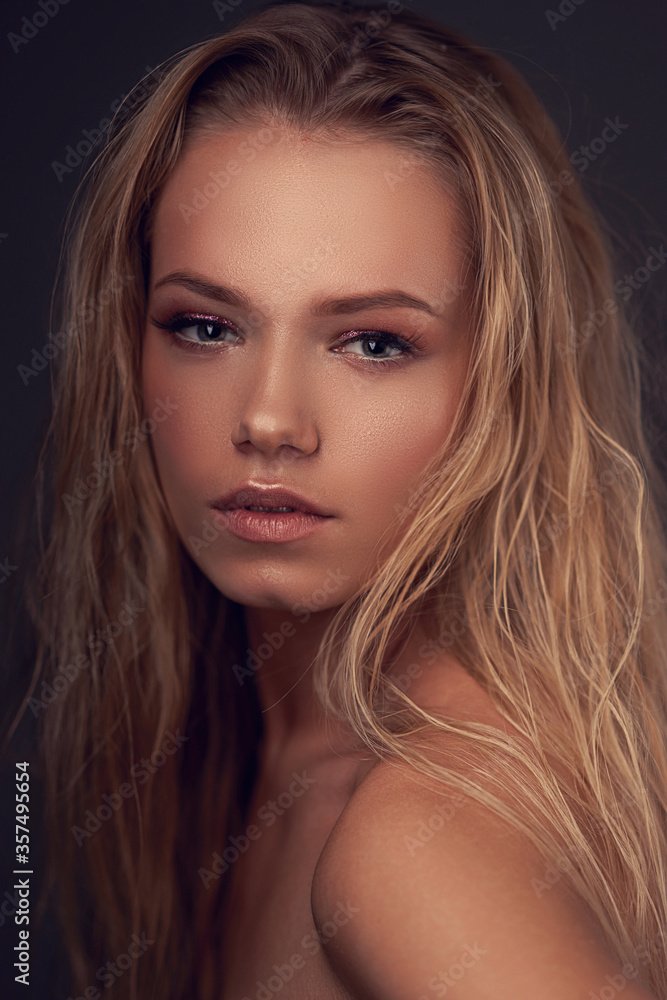 Obraz premium Closeup face portrait of young pretty caucasian woman with long blonde woman looking in camera and posing against gray background. Shallow DOF.