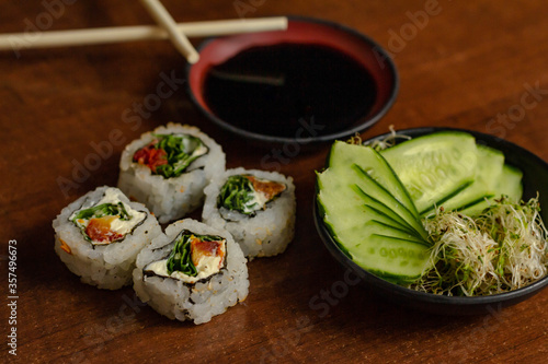Sushi uramaki de rúcula com tomate seco e cream cheese acompanhado de shoyu, salada de pepino e broto de feijão