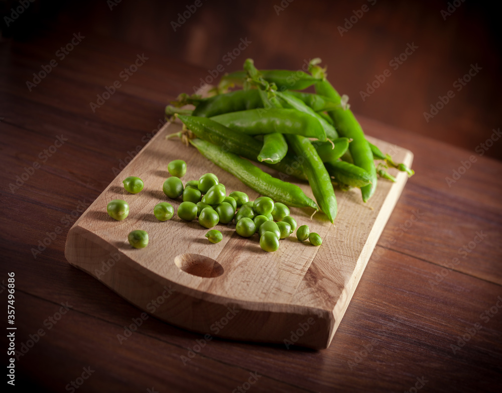 Peas slanted fresh arrangement on cutting board and wooden table dark background front view studio shot