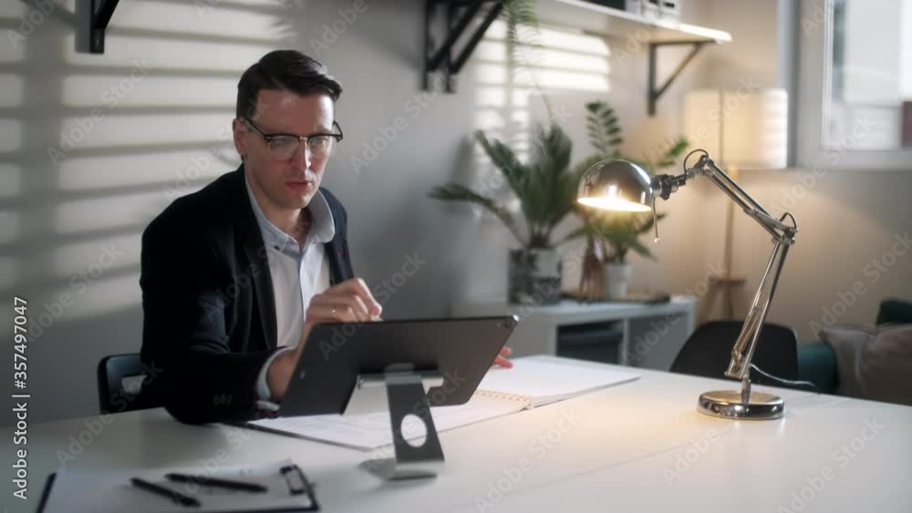 Business Man Engineer Is Working With Blueprints And Laptop In Modern Workplace. Handsome Male is Glasses Working In Modern Office Interior Work Place, Looking Concentrated And Confident. Business Man Engineer Is Working With Blueprints And Laptop In Modern Workplace. Handsome Male is Glasses Working In Modern Office Interior Work Place, Looking Concentrated And Confident.