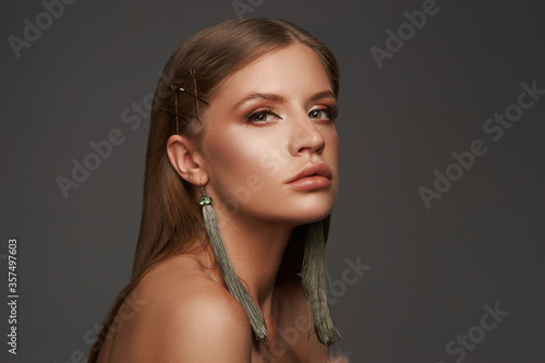 Beautiful young woman with long dark straight hair. Brunette with perfect makeup wearing long green earrings closeup portrait against gray background